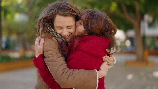 Mother and daughter kissing and hugging each other standing at park