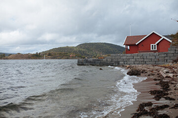 Norwegian wooden red house on the seashore.  Landscape of the Norwegian coast. Norwegian mountains.
