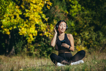 Young asian fit woman sitting on mat in lotus position meditating relaxing and listening to music...