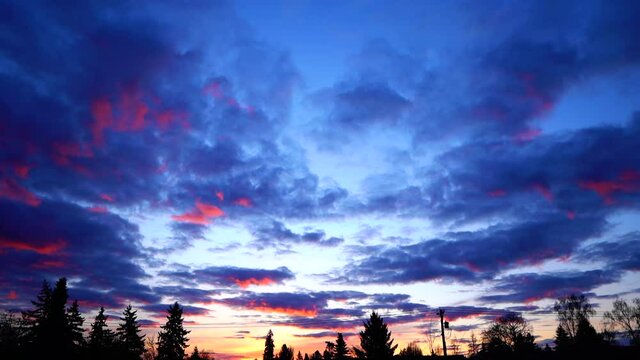 Partially cloudy sunrise time lapse over neighborhood outside of a bedroom window with orange, pink  and blue colors