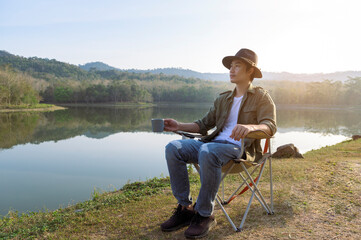 Fototapeta premium Traveler man is drinking hot coffee over mountain and river view , concept of camping , nature tourism .