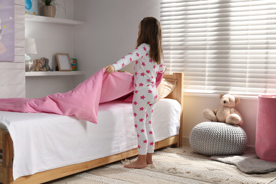Cute little girl making bed at home