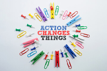 Text sign showing Action Changes Things with office stationery clips and pins around forming a circle