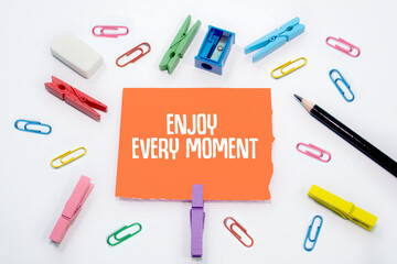 Text sign showing Enjoy Every Moment on Set of colorful paper clips with white copy space background.