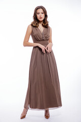 Naklejka premium High fashion photo of beautiful elegant young woman in a pretty beige brown dress with a neckline, necklace posing on white background. Slim figure, make up, luxurious hair, shiny curls. Studio Shot