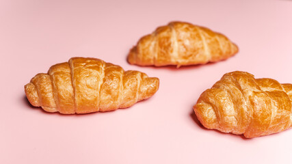 Three fresh-baked crispy golden buttery croissants isolated on pink background with copy space. Pastry and dessert studio shot.