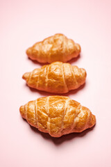 Three fresh-baked crispy golden buttery croissants isolated on pink background with copy space. Pastry and dessert studio shot.
