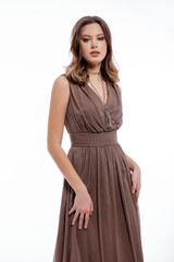 Naklejka premium High fashion photo of beautiful elegant young woman in a pretty beige brown dress with a neckline, necklace posing on white background. Slim figure, make up, luxurious hair, shiny curls. Studio Shot