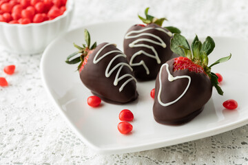 Chocolate covered strawberries on a plate with cinnamon hearts scattered around.