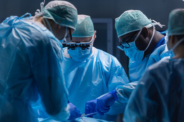 Fototapeta Multiracial team of professional medical surgeons performs the surgical operation in a modern hospital. Doctors are working to save the patient. Medicine, health, cardiology and transplantation. obraz