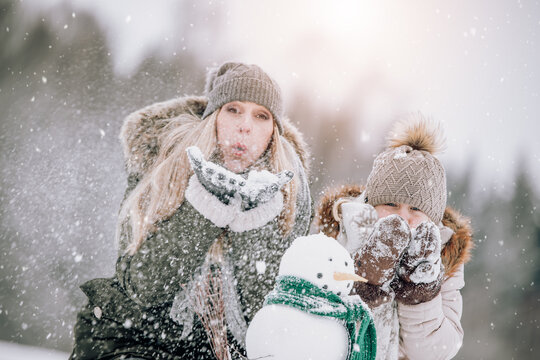 parent and child blowing snow in wintertime