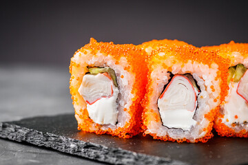appetizing sushi roll california with cheese cucumber crab and masago caviar on a black stone plate