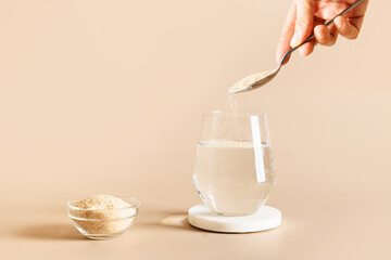 Woman adds psyllium fiber to glass of water on beige background. Superfood for healthy intestines...