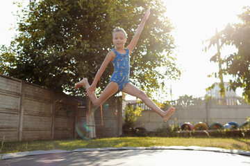 little sports girl jumps on a trampoline. Outdoor shot of girl jumping on trampoline, enjoys jumping in home. happy summer vacation