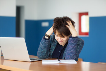 businesswoman sits at table with laptop, looks at notebook and gets upset. negative emotions, problem