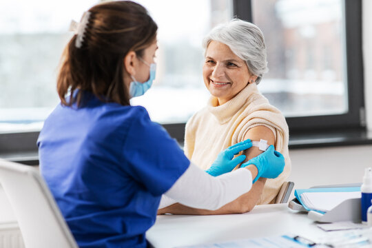 medicine, health and vaccination concept - doctor or nurse applying medical patch to vaccinated senior woman at hospital