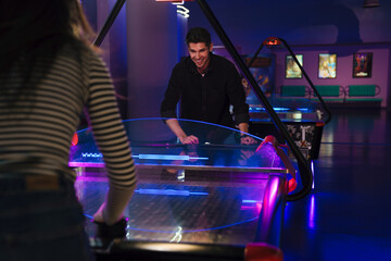 Young man and woman smiling while playing air hockey