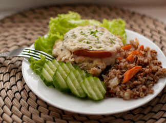 buckwheat, chop with sauce and sliced cucumber on a plate on a woven napkin with blurred edges