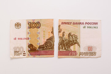 a hundred-ruble Russian banknote, torn into two parts on a white background