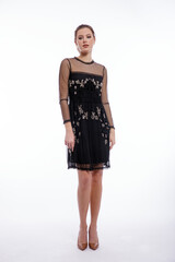 High fashion photo of a beautiful elegant young woman in a pretty black dress with lace posing on white background. Studio shot. Slim figure, hair is gathered in a ponytail
