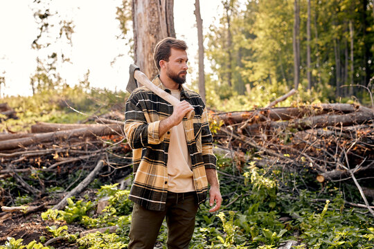 Lumberman work with ax in summer forest. Strong lumberjack in plaid shirt look at side. Stylish handsome caucasian lumberman getting ready for work. Lifestyle. Hard work in forest. Illegal logging