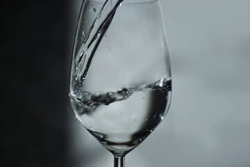 A stream of clean water is poured into a glass from a bottle close-up on a light, gray background