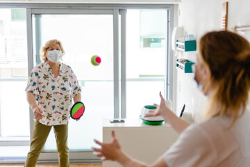 occupational therapist or kinesiologist rehabilitating shoulder tendinitis in an elderly woman with a ball catching exercise in the air