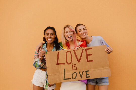 Young lesbian girls smiling and holding banner over yellow wall