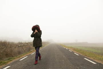 Obraz premium Chica con frío con abrigo caminando con niebla por una carretera secundaria, huida 