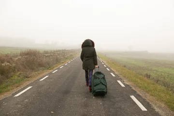 Fotobehang Con una bolsa maleta una mujer camina por la carretera con mucha niebla, parte trasera © Imagen Punto de Luz