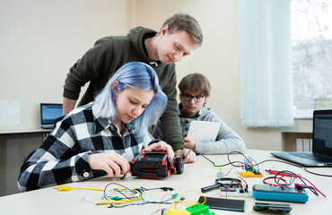 Diverse teenager pupils build robot vehicle learning at table at STEM engineering science education...