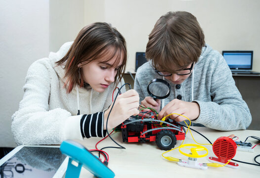 School student making robotic cars. Teenager girl and boy at robotics school makes robot managed from the constructor, child learns robot constructing.