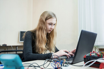 Teenager girl works at laptop, collects and programs the robot. STEM and STEAM education.