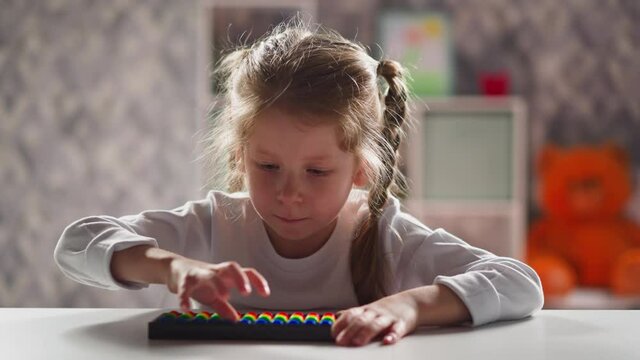 Serious little schoolgirl with blonde thin braids learns to do sums with abacus at home mental arithmetic lesson close view slow motion