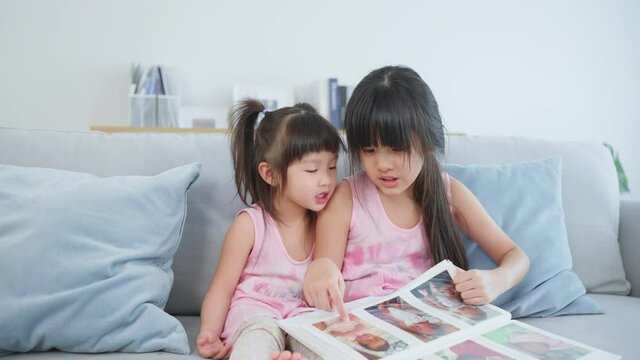 Asian big sister showing old album recalls the past to younger sibling. 