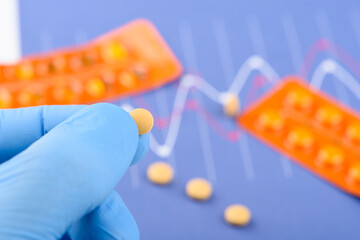 Scientist hold small pill in a hand with blister packs on background