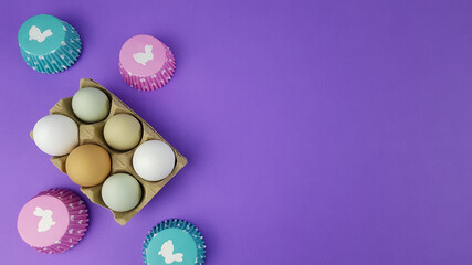 colorful Easter eggs on a very peri background. nearby there are baking pans of pink and blue cupcakes