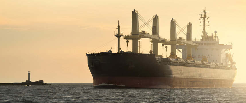 Large cargo ship (bulk carrier, 179.99 meters length) sailing in the Baltic sea at sunset. Freight transportation, logistics, global communications, economy, industry, supply, environment