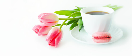 three pink tulips, macarons and a cup of coffee on a white table..