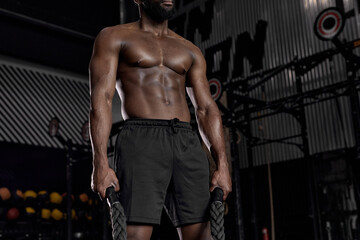 Fototapeta na wymiar Workout. Crossfit. Extreme. Training. Cropped shirtless muscular man posing at camera, holding heavy battle ropes for cross fit training, black man has strong abs muscles, in perfect physical shape