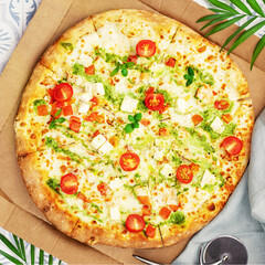 Natural italian big pesto pizza with thin dough, chicken, mozzarella, cherry tomatoes and bazil in a craft box with palm leaves. Mediterranean cuisine. Healthy and testy fast food