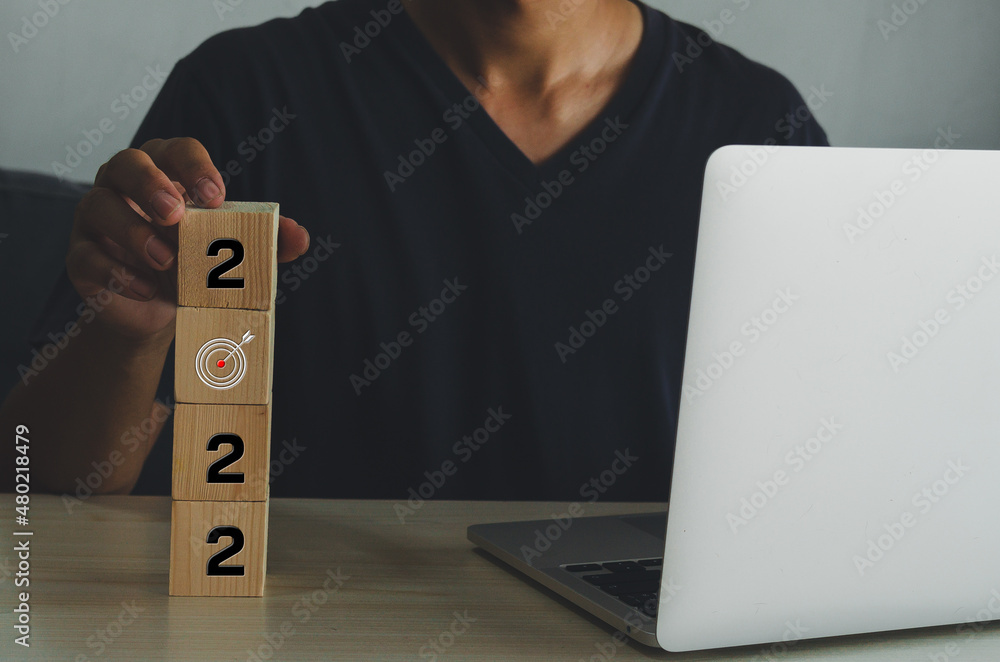 Poster man holding cube wooden target numeber 2022 working on a desk with a computer. business idea.