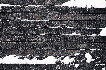 Part of the wooden wall of a burnt house covered in snow. Burnt wood texture