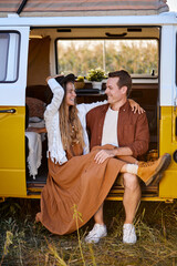 Attractive young couple sitting inside of campervan while looking outside of the van, man and woman have talk, laughing, enjoying summer evening in countryside nature. travel, people lifestyle