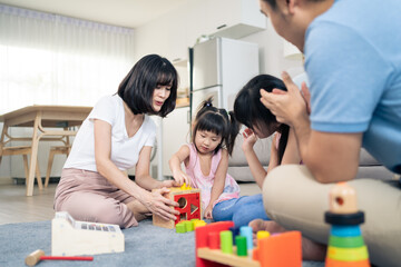 Asian happy family sit on floor, play kid toy together in living room. 