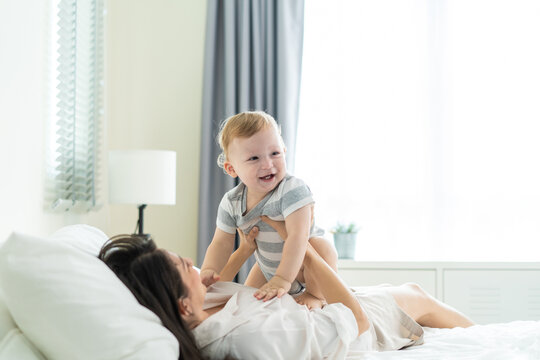 Caucasian loving mother playing with baby boy child on bed in bedroom. 