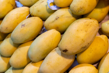 Mango, a photo of fresh yellow mango pile on market table. Ripe tropical fruit closeup. Asian fruit market stall in Thailand