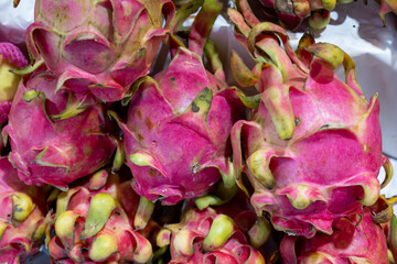 Dragon fruits, a photo of fresh dragon fruit pile on market table. Ripe tropical fruit closeup. Asian fruit market stall in Thailand