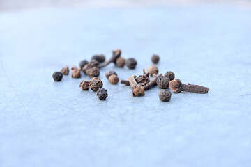 closeup the bunch black peppers with brown cloves over out of focus grey background.