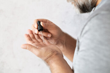 Natural mustache and beard oil. A man applies oil to his beard with a glass pipette.